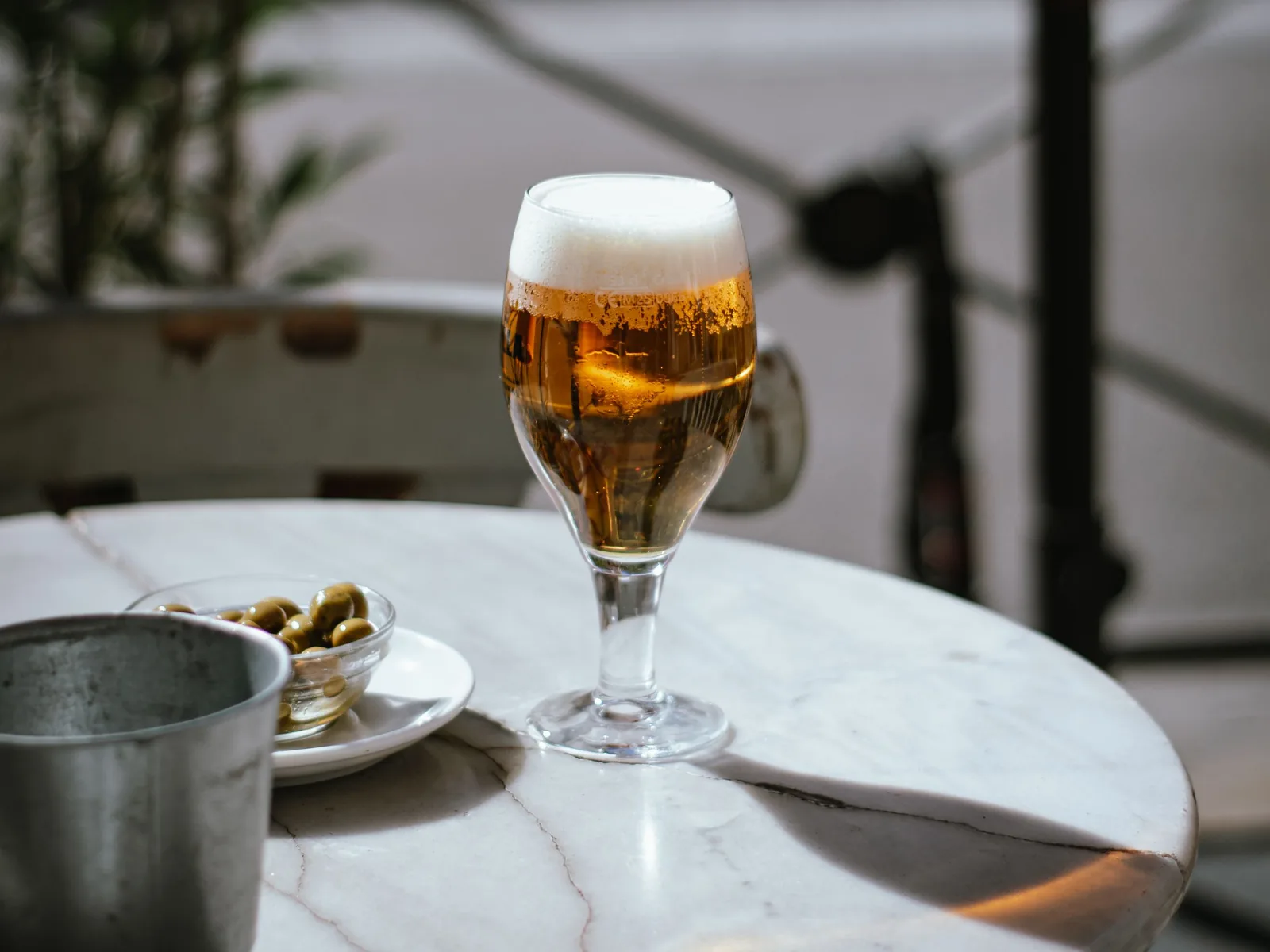 Ein Glas Bier und ein Schälchen Oliven auf einem runden Marmortisch einer Bar