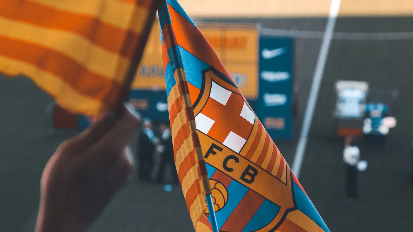 Eine Hand schwenkt im Stadion eine Fahne mit dem Wappen des FC Barcelona, daneben die katalanische Flagge