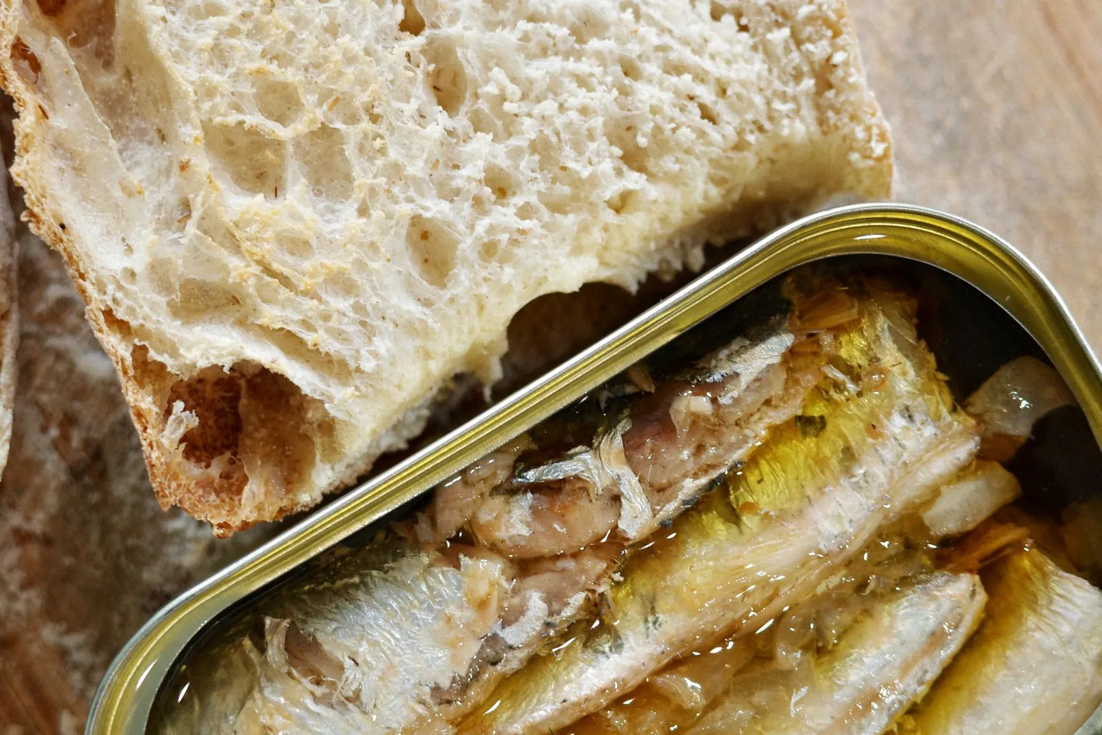 Eine geöffnete Dose Sardinen in Öl neben einer Scheibe Landbrot