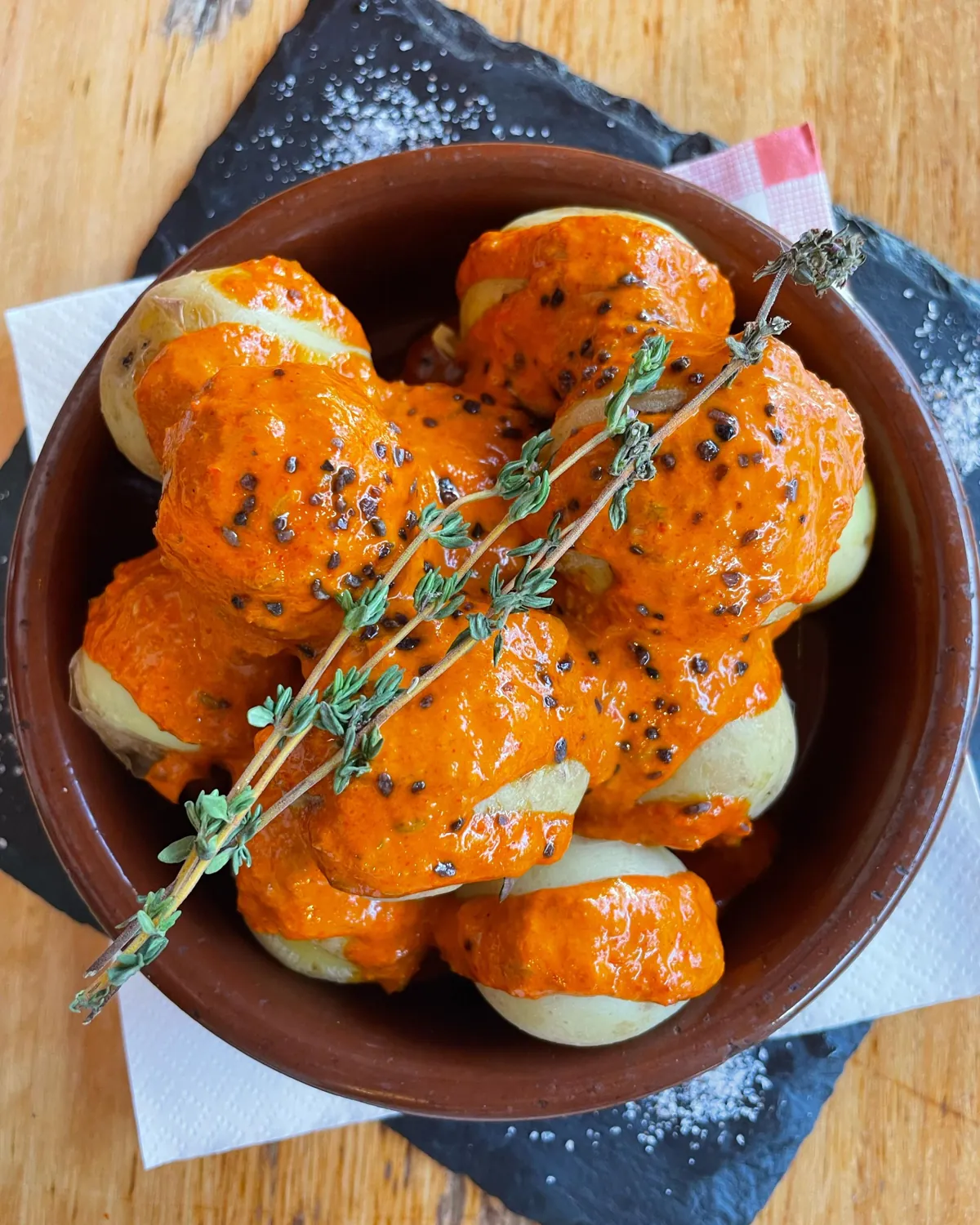 Papas arrugadas mit rotem Mojo in einer Tonschale, darüber ein Thymianzweig