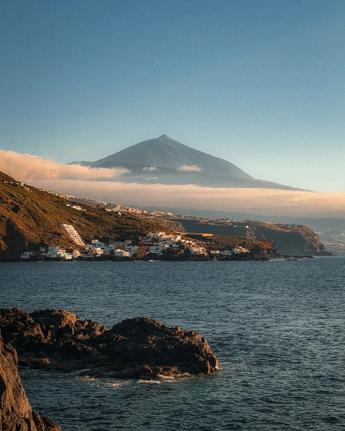 Der Teide über einem Wolkenband, davor die felsige Nordküste Teneriffas und der Atlantik im Abendlicht