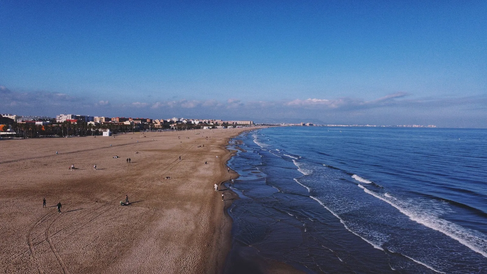 Luftbild der Küste von Valencia: breiter Sandstrand, Wellen des Mittelmeers und die Stadt am Horizont